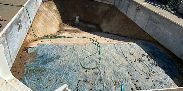 An empty swimming pool under renovation with a hose and debris inside.