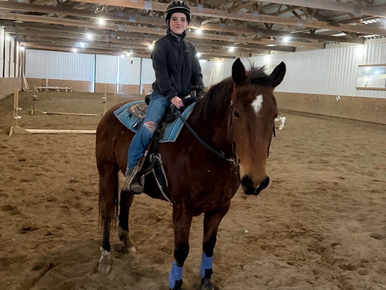 A person wearing a helmet rides a horse in an indoor arena.