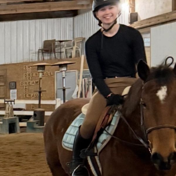 Smiling rider on a brown horse inside an indoor riding arena.
