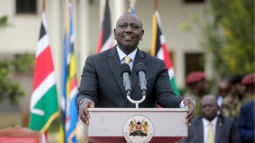 Kenyan leader speaking at a podium with national flags in the background.