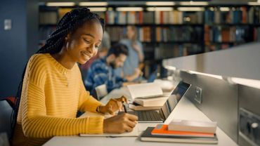 Young woman studying with a laptop in a library.