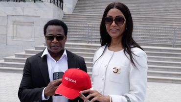Two people holding a red cap with 'FREE SOKA' text, standing outdoors near stairs.