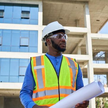 Construction worker in safety gear holding blueprints at site.