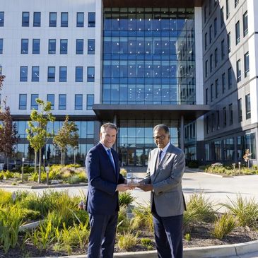 Two men in suits exchanging an award outside a modern office building.