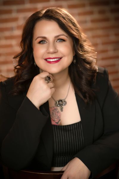 Smiling woman with dark hair and tattoo, wearing black blazer.