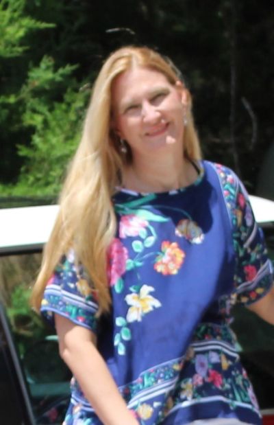 Smiling woman with long blonde hair in a blue floral dress.