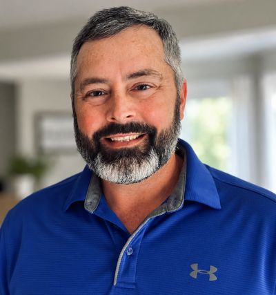 Smiling man with beard in blue polo shirt indoors.