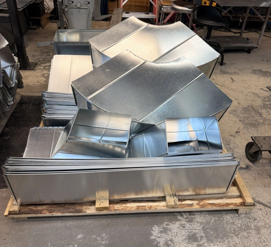 Shiny metal ductwork components on wooden pallet.
