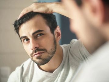 Man pulling back his hairline looking closely