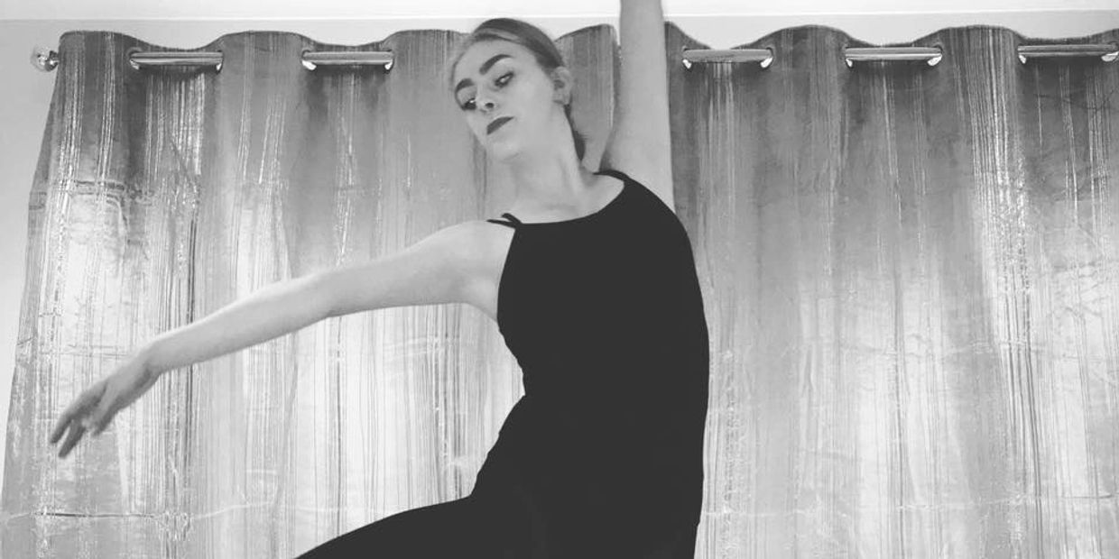 Tiegan Liebscher in front of a curtain in her black unitard, practicing a ballet retire position. 