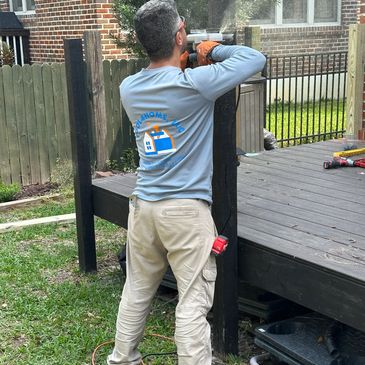 Worker sanding a wooden post on a deck in a backyard.