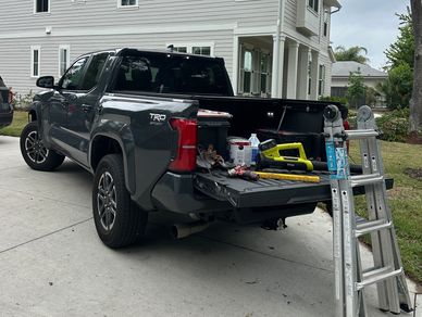 Pickup truck with tools and ladder on driveway near a house.