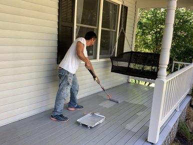 Man painting a wooden porch floor gray with a roller.