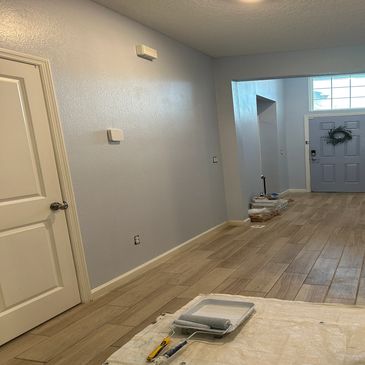 Hallway with light blue walls, wood-look tile floor, and painting supplies on a drop cloth.