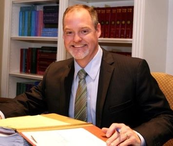 Man in suit smiling at desk with documents.