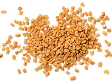 Heap of fenugreek seeds scattered on a white background.