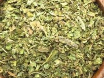 Dried green leaves in a wooden bowl, likely an herb or tea.