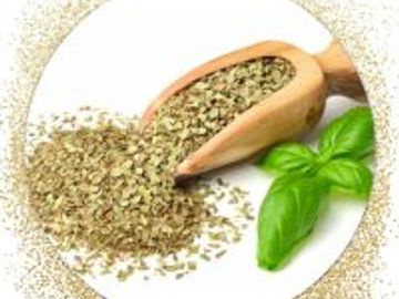 Dried oregano spilling from a wooden scoop with fresh basil leaves on a white plate.