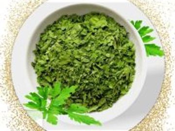 Bowl of dried green herbs garnished with fresh parsley leaves.