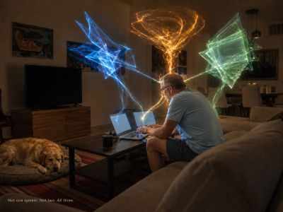Man at laptops as three colored light forms converge on him.