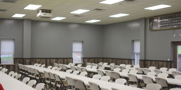 Empty conference room with rows of white chairs and tables.