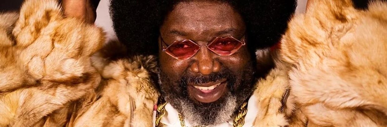 Man with afro and red glasses wearing a fur coat, smiling.