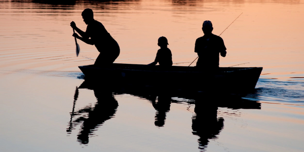 Silhouettes of three people fishing from a boat at sunset.