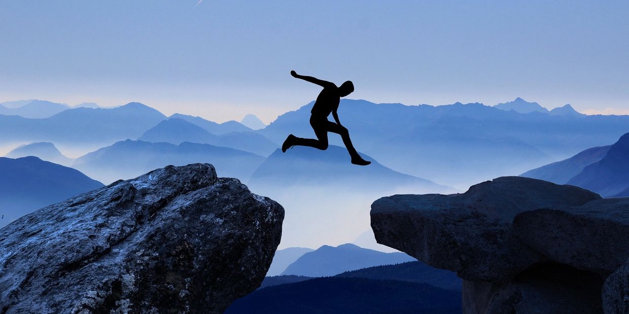 A person jumping between to boulders with a blue background