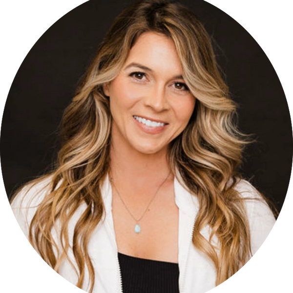 Smiling woman with long wavy blonde hair wearing a white jacket and necklace.