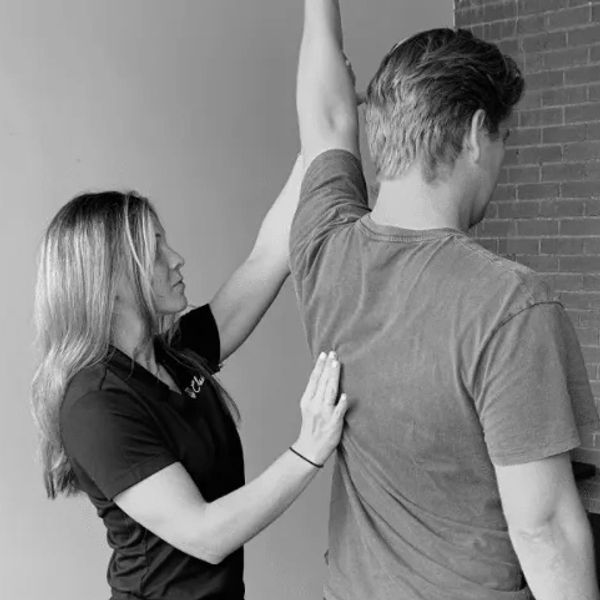 A woman assists a man with arm stretching exercises indoors.