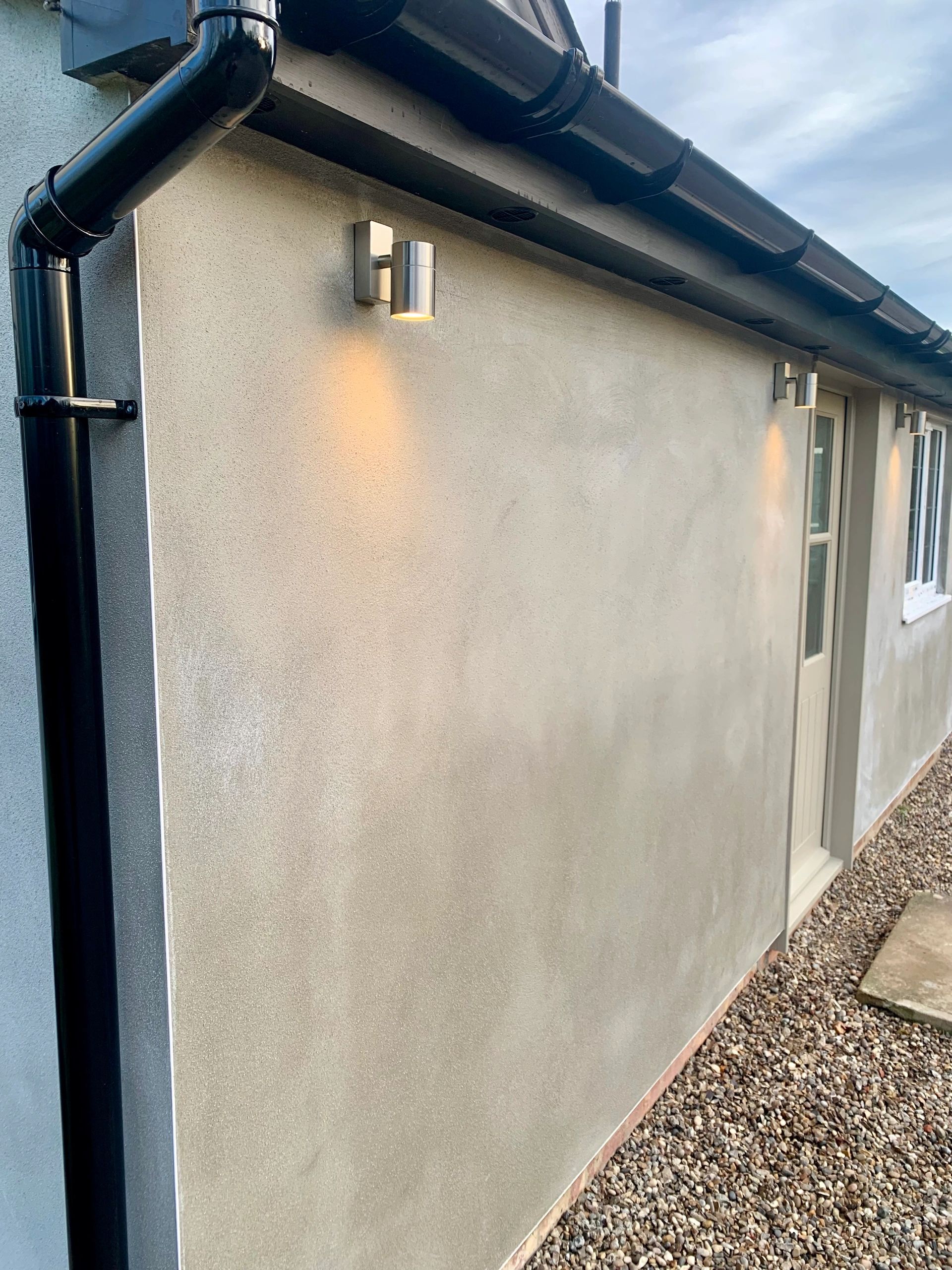 Outdoor wall lights illuminate a smooth beige exterior wall with black gutters above.