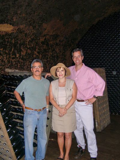 Three people posing in a wine cellar with stacked bottles in the background.