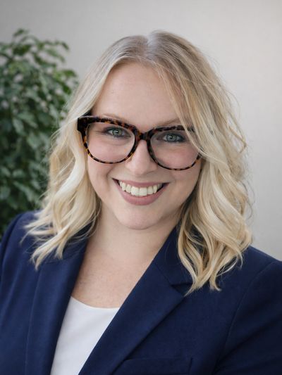 Smiling woman with blonde hair and tortoiseshell glasses in a navy blazer.