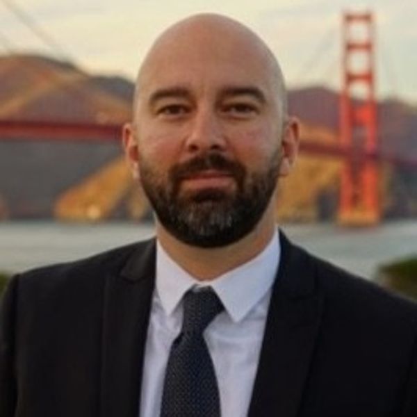 Man in a suit posing with the Golden Gate Bridge in the background.