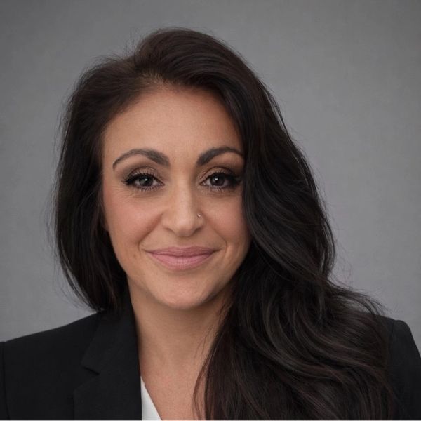 Professional woman with long dark hair and a confident smile in a black blazer.