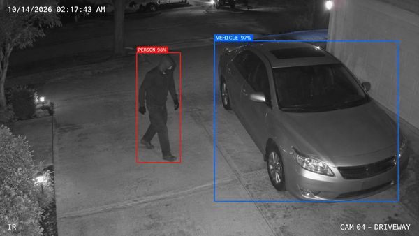 Person walks near parked car at night in driveway.