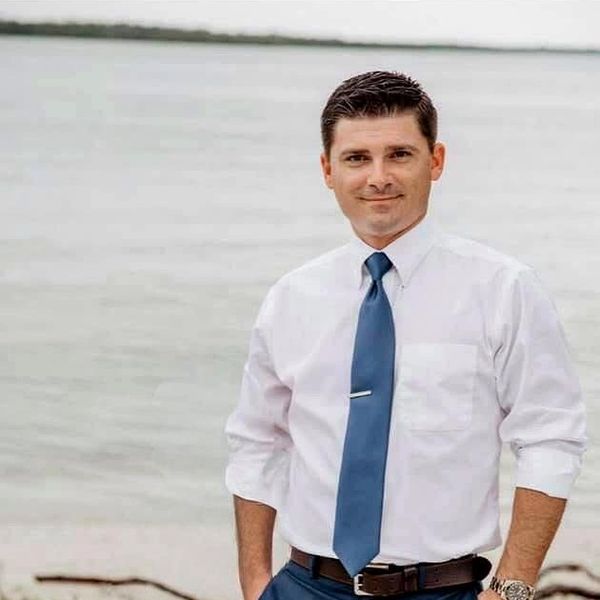 Man in white shirt and blue tie standing by a body of water.
