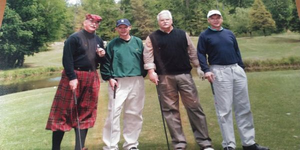 Four men posing with golf clubs on a lush green golf course.