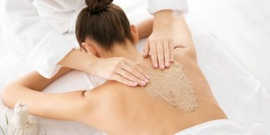 Therapist applying exfoliating scrub on woman's back during spa treatment.