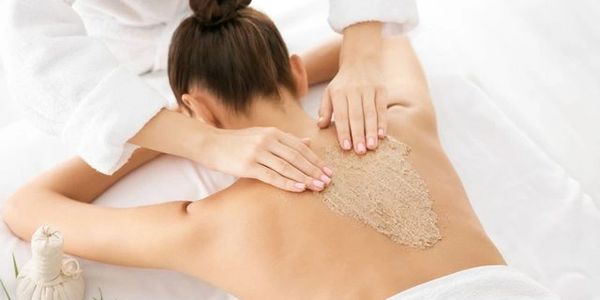 Therapist applying exfoliating scrub on woman's back during spa treatment.