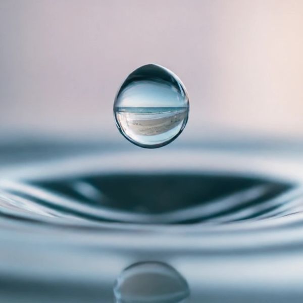 A water droplet suspended over rippling water.