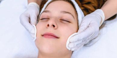 Woman receiving a gentle facial massage with cotton pads.