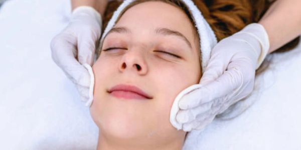 Woman receiving a gentle facial massage with cotton pads.