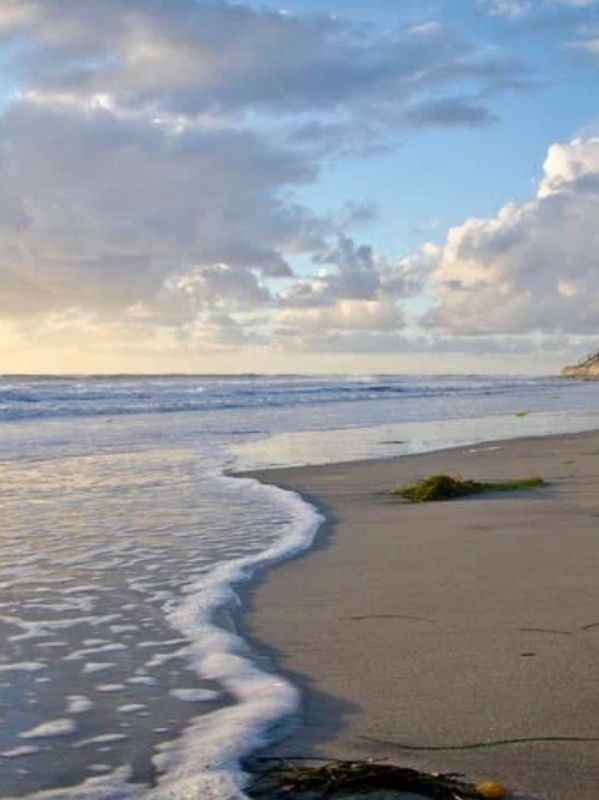 Gentle waves washing onto a sandy beach under a cloudy sky.