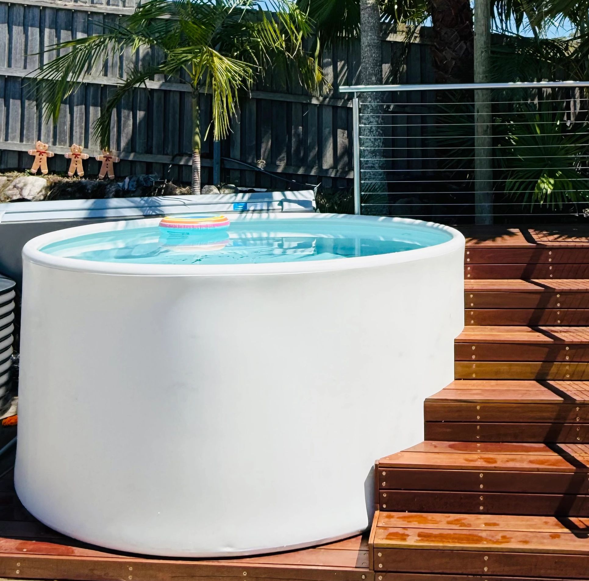 Outdoor round pool with wooden stairs and tropical plants.