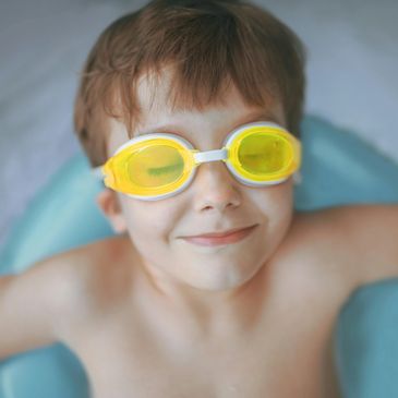 Young boy smiling with yellow swimming goggles, eyes closed.