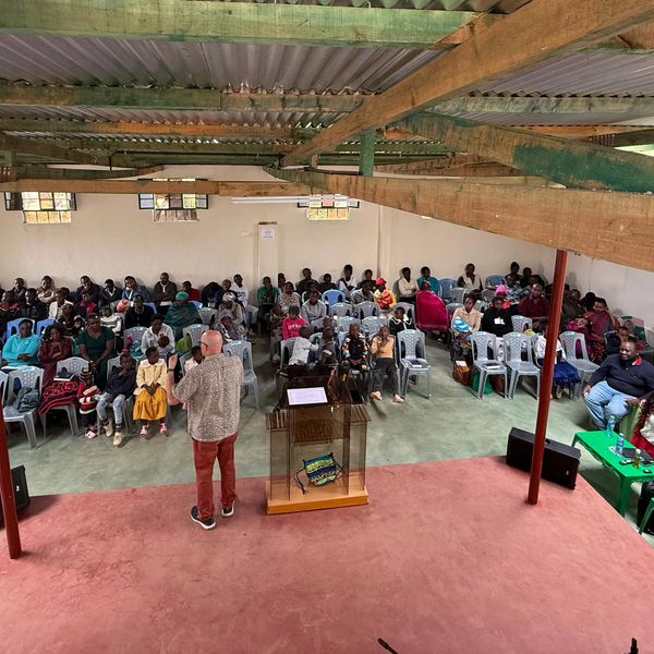 Man speaking to seated audience in a community hall.