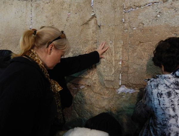 Two women pray at the Western Wall placing notes into cracks.