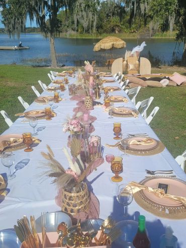 Outdoor dining setup by the lake with a white tablecloth and pink accents.