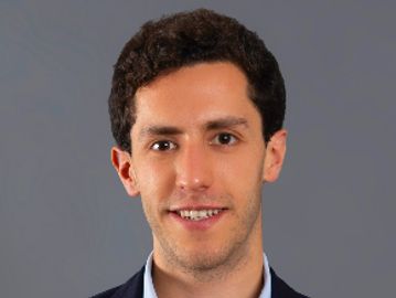 Portrait of a young man with dark curly hair and a subtle smile.